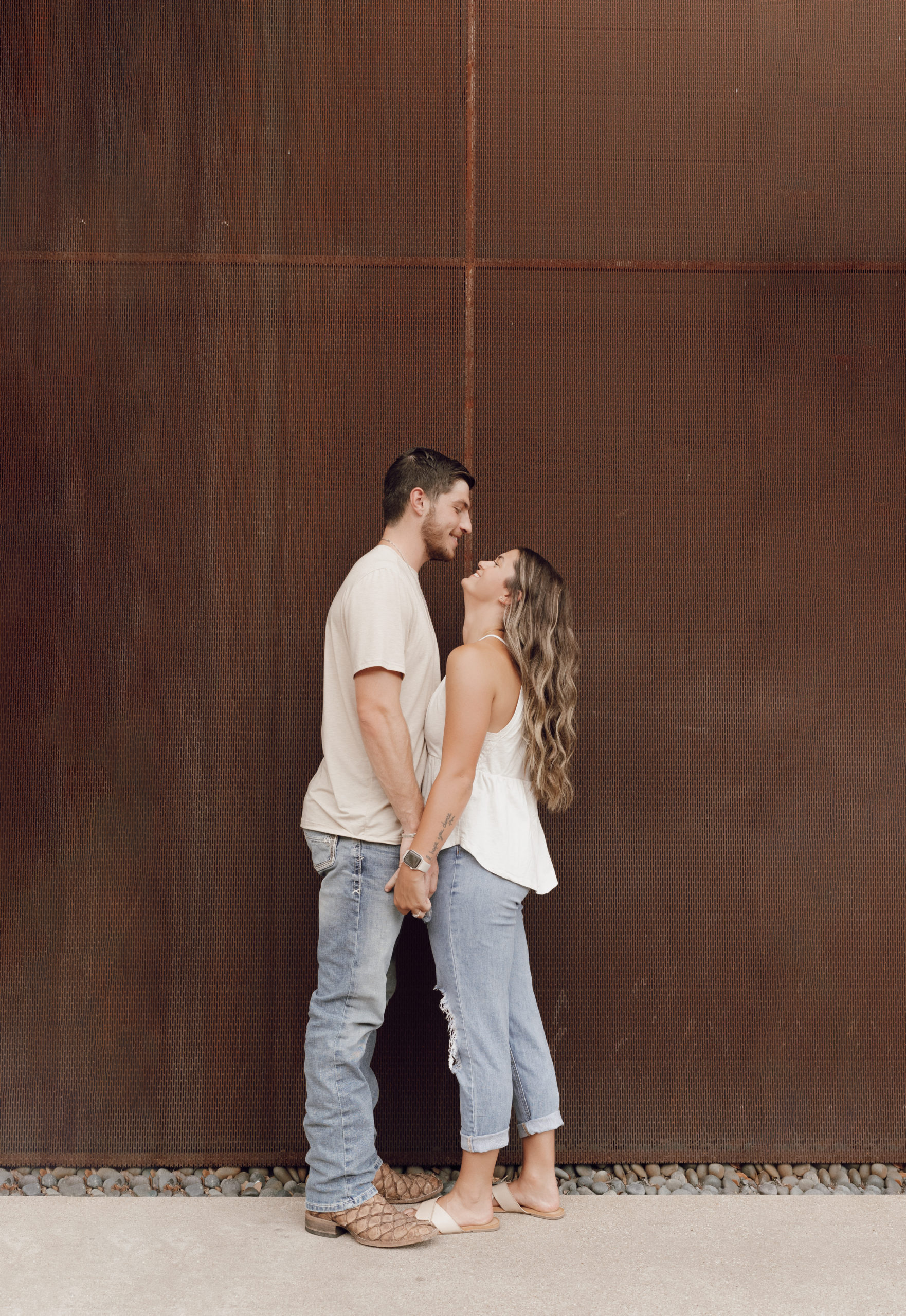Couple cuddles up in front of a rust metal wall.