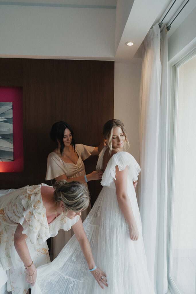 bridesmaid and mother helping bride with wedding dress