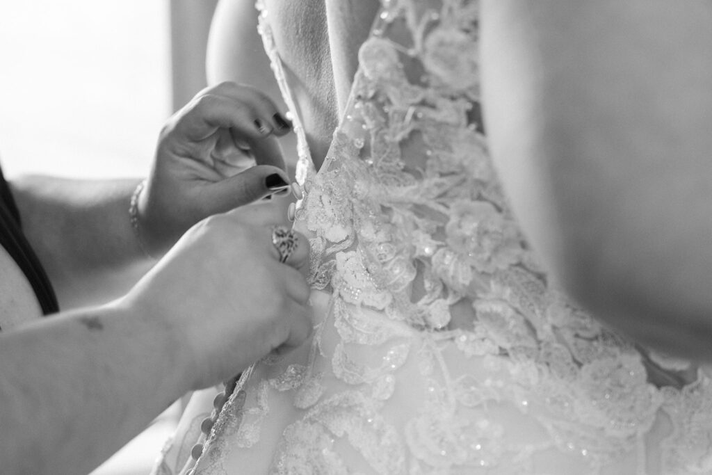 brides mother helping her button the back of her lace wedding dress